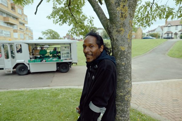 Man on crutches leans on tree in front of food hub van 