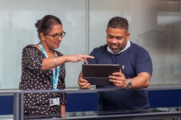 A man holds and ipad and a woman points at it